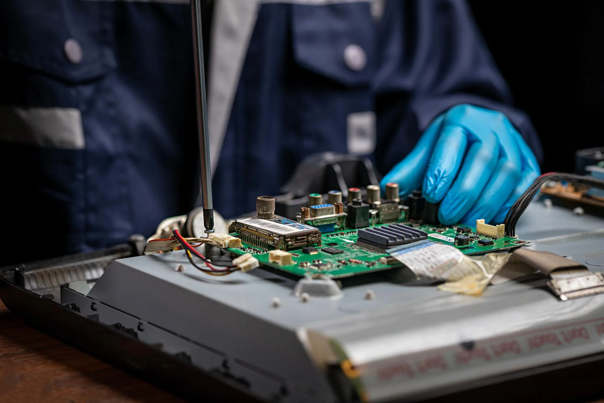 Close-up of a blue-gloved technician diagnosing the monitor's controller board with a precision screwdriver