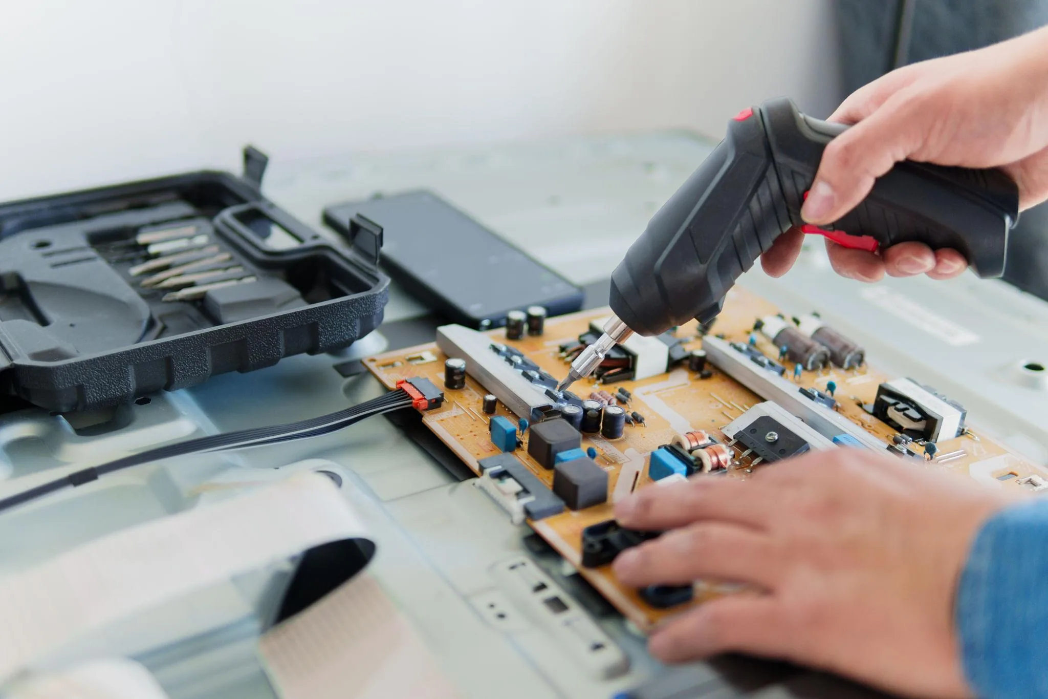 Hands using a cordless driver to replace electrolytic capacitors on a computer monitor power supply board