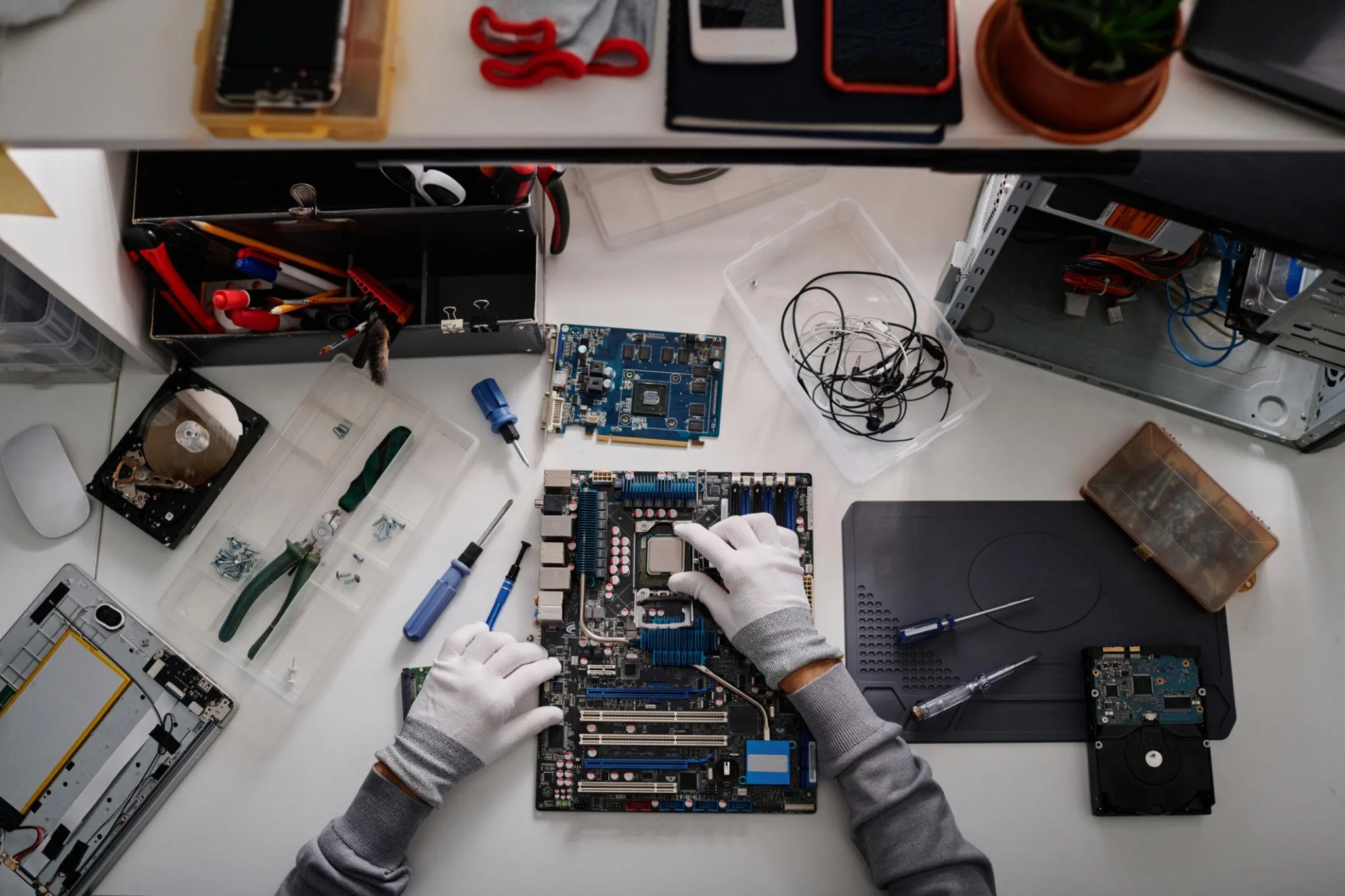 Top-down view of a technician's desktop repair workbench with motherboard, screwdrivers, hard drives and organised tool tray