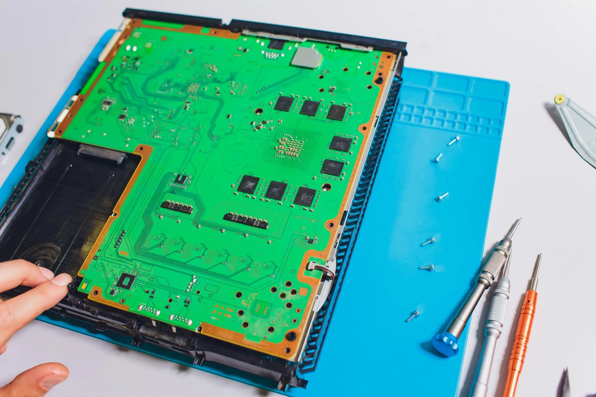PlayStation 5 motherboard removed from the chassis on a blue silicone repair mat with screws laid out and precision screwdrivers ready