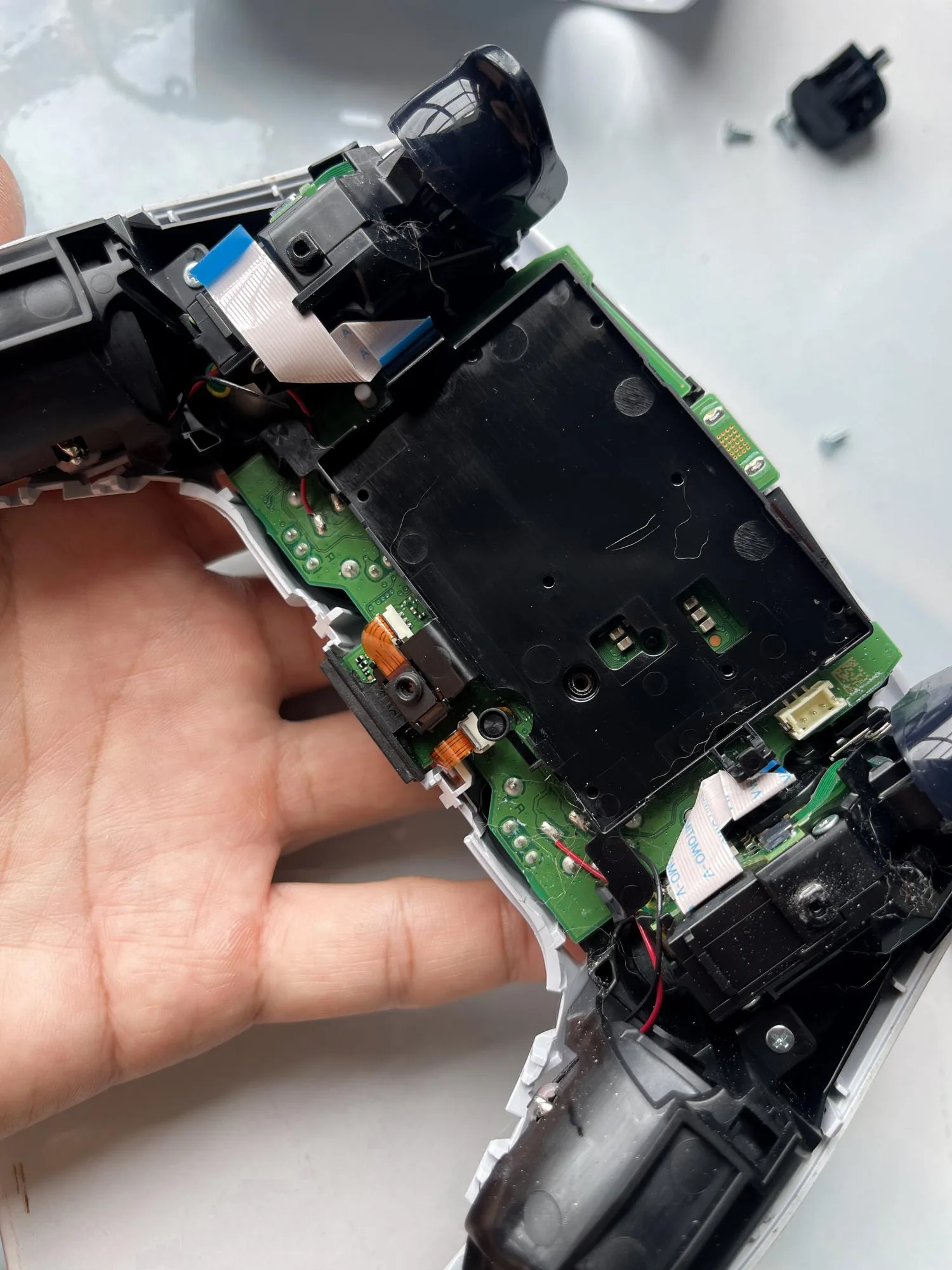 Internal teardown of a game controller showing exposed circuit board, ribbon cables and analog stick modules