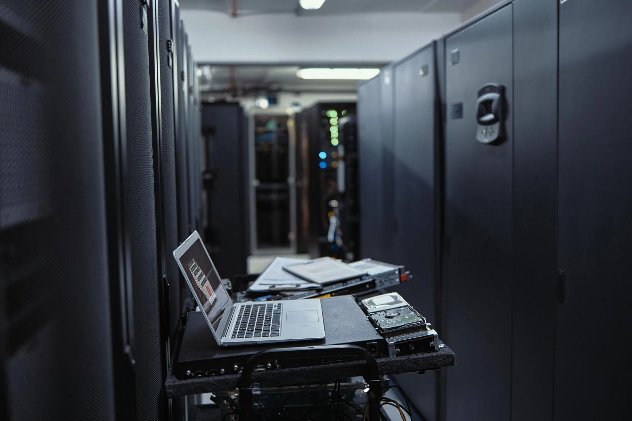 Open laptop on a service trolley inside a darkened server room with rack equipment around it, used by an IT technician for diagnostics
