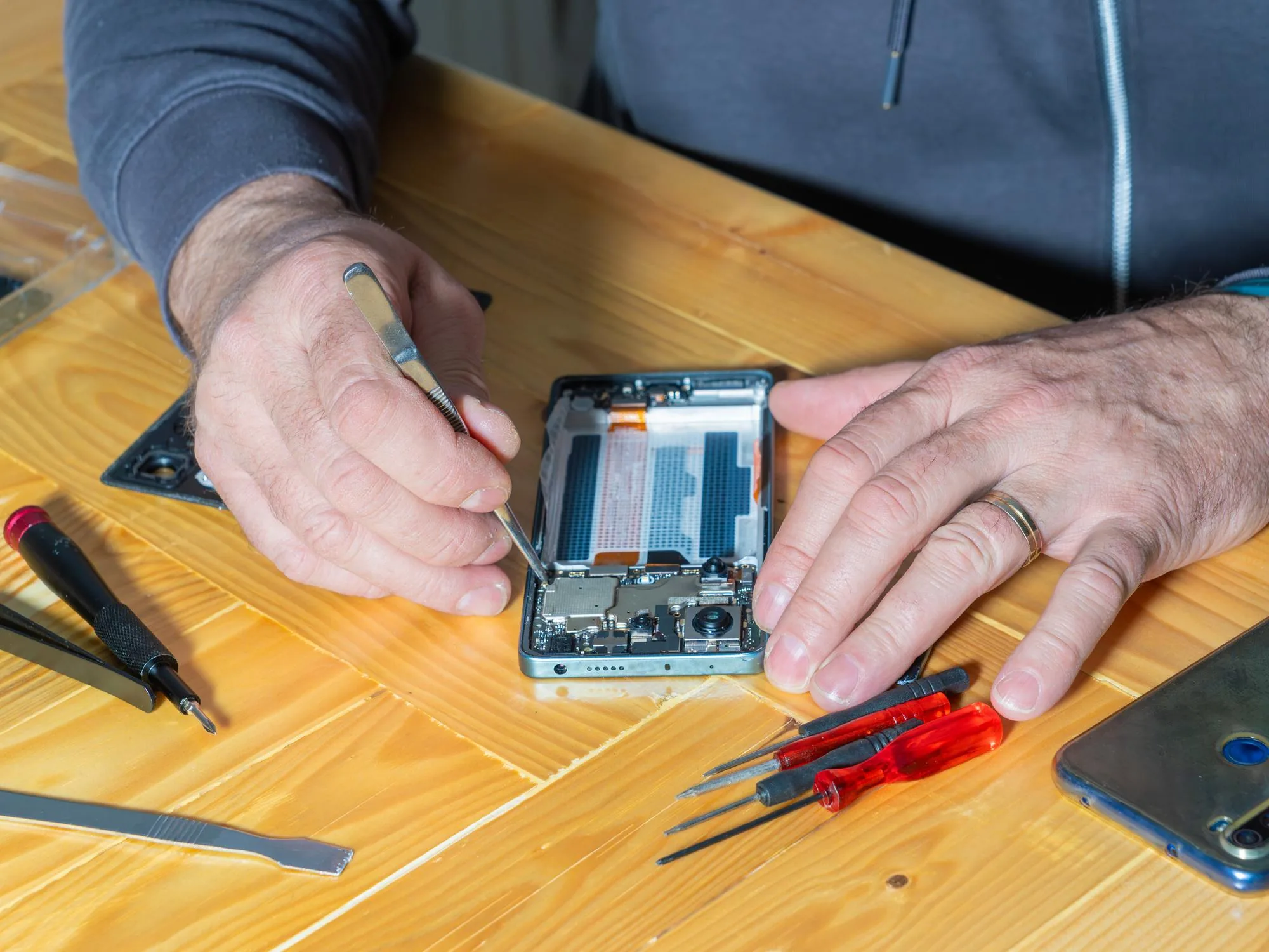 Hands lifting a smartphone display panel after softening the perimeter adhesive
