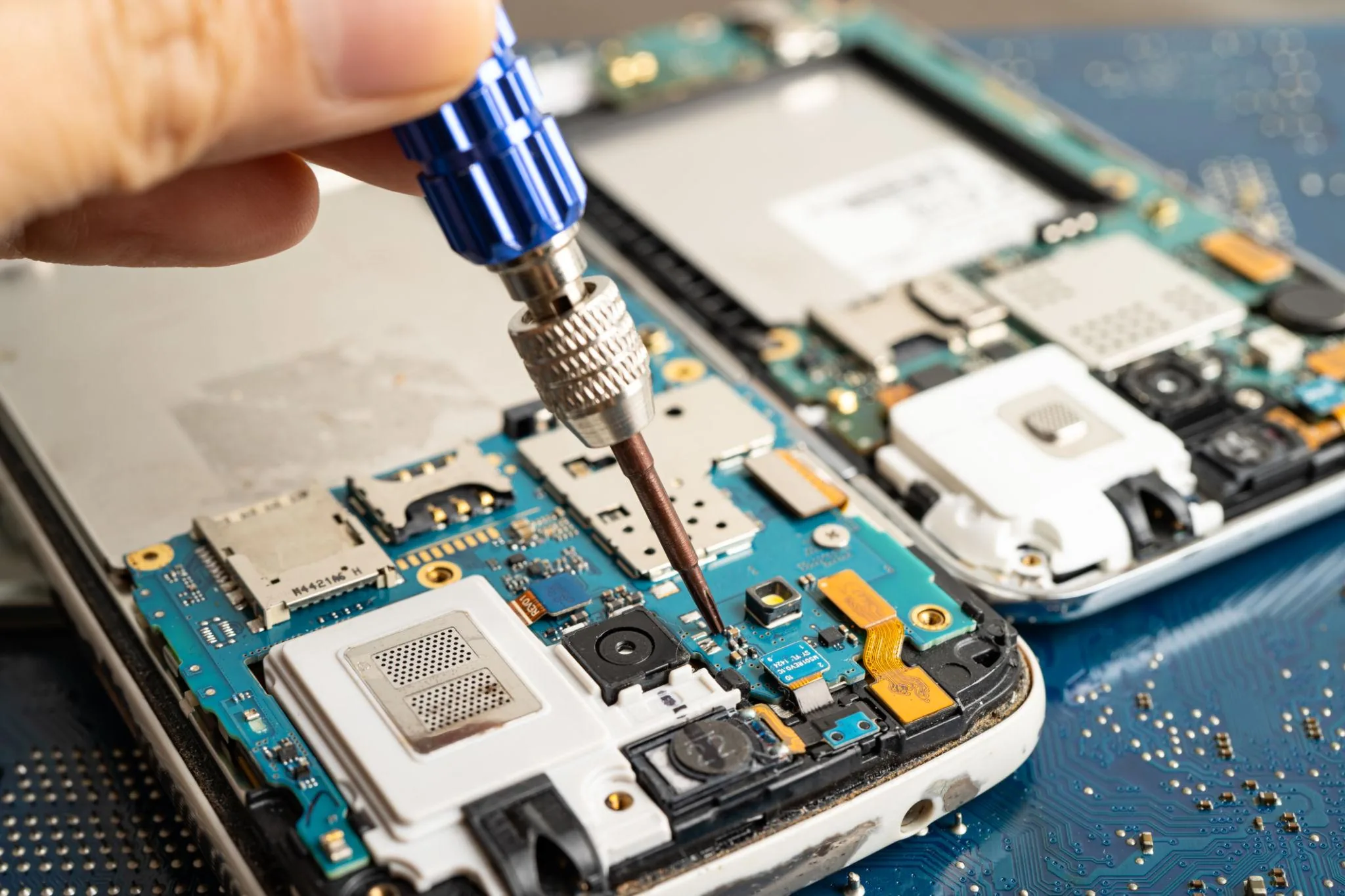 Precision screwdriver releasing the metal shield over the display ribbon connectors on a smartphone